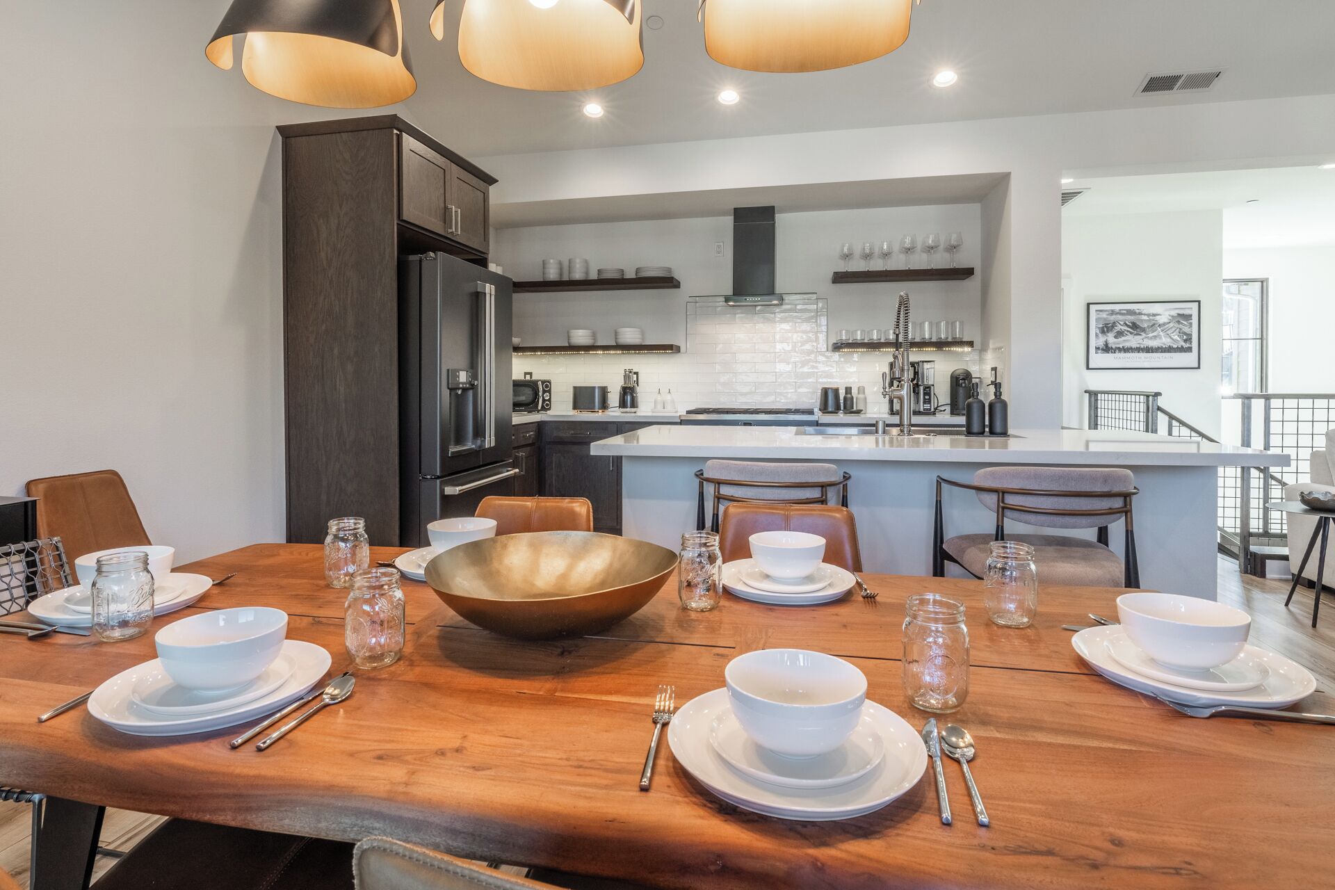 A modern kitchen with dark wood cabinets, a central island, and a dining area set for six with white plates, bowls, and cutlery.