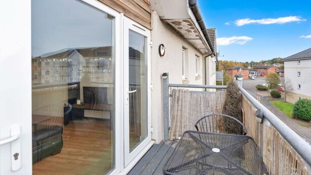 A balcony with a table and chairs, a sliding glass door, and a view of a residential area.