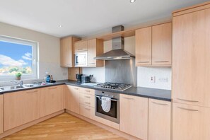 A modern kitchen with wooden cabinets, a gas stove, a microwave, and a stainless steel range hood. - Free Parking | Central | 2 Bedroom | 4 Guests (West Lothian)