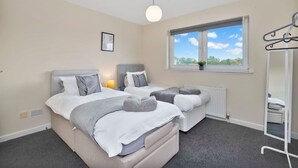 A bedroom with two beds, a window with a view, a radiator, and a hanging coat rack.