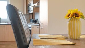 A modern kitchen with wooden cabinets, a dining table with a vase of sunflowers, and a black chair.