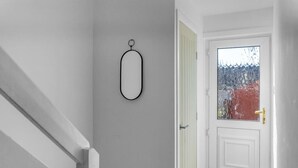 A hallway with a white door, a small oval-shaped object on the wall, and a window with a view of trees.