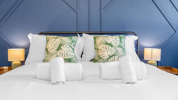 A bed with white bedding, two green and white leaf-patterned pillows, and two white towels.