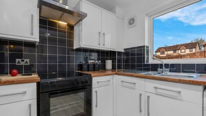 A modern kitchen with white cabinets, a black stove, and a window overlooking a residential area. - Free Parking | Central | Sleeps 5 | 2 Bedrooms (West Lothian)