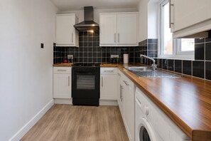 Una cocina compacta con armarios blancos, estufa negra y encimera de madera.