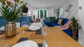 A dining area with a wooden table set for two, a vase with flowers, and a blue sofa in the background. - Free Parking | Central | Sleeps 5 | 2 Bedrooms (West Lothian)