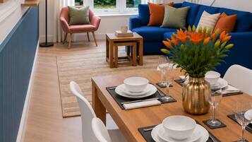Un coin repas avec une table en bois dressée pour quatre personnes, des chaises blanches et un vase rempli de fleurs.