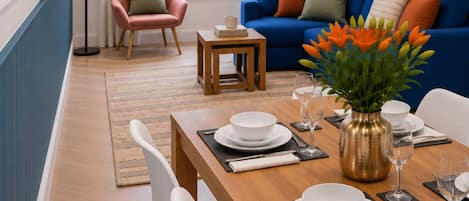 Un coin repas avec une table en bois dressée pour quatre personnes, des chaises blanches et un vase rempli de fleurs.
