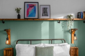 A bedroom with a green wall, a metal bed frame, white bedding, and two bedside tables with wall-mounted lamps.