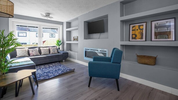A modern living room with a grey sofa, a blue armchair, a flat-screen TV, and a fireplace.