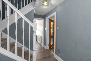 Un couloir avec un escalier en bois, une porte dotée d’un panneau en verre et un luminaire au plafond.
