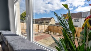 A room with a large window, a bench, and a view of a backyard with a wooden fence and houses.