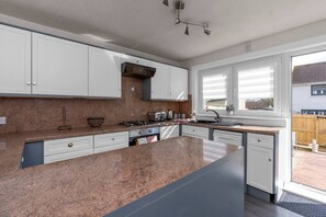 Eine moderne Küche mit weißen Schränken, einer Granit-Arbeitsplatte, einem eingebauten Backofen und einem Fenster mit Jalousien.