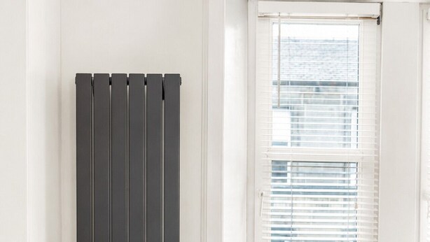 A room with a radiator, a window with blinds, a cushioned bench, and a wooden table with a plant. - Stunning 1-Bedroom Flat in Edinburgh | Sleeps 3 (Edinburgh)