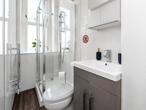 Ein modernes Badezimmer mit Duschkabine aus Glas, einer weißen Toilette und einem Waschbecken mit Spiegel darüber.