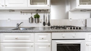 Una cucina con mobili bianchi, un piano di lavoro in granito, un lavello in acciaio inox, un fornello a gas e un forno integrato.