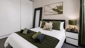 Una camera d'albergo con un letto, un comodino, una lampada, un quadro e una finestra con tende.