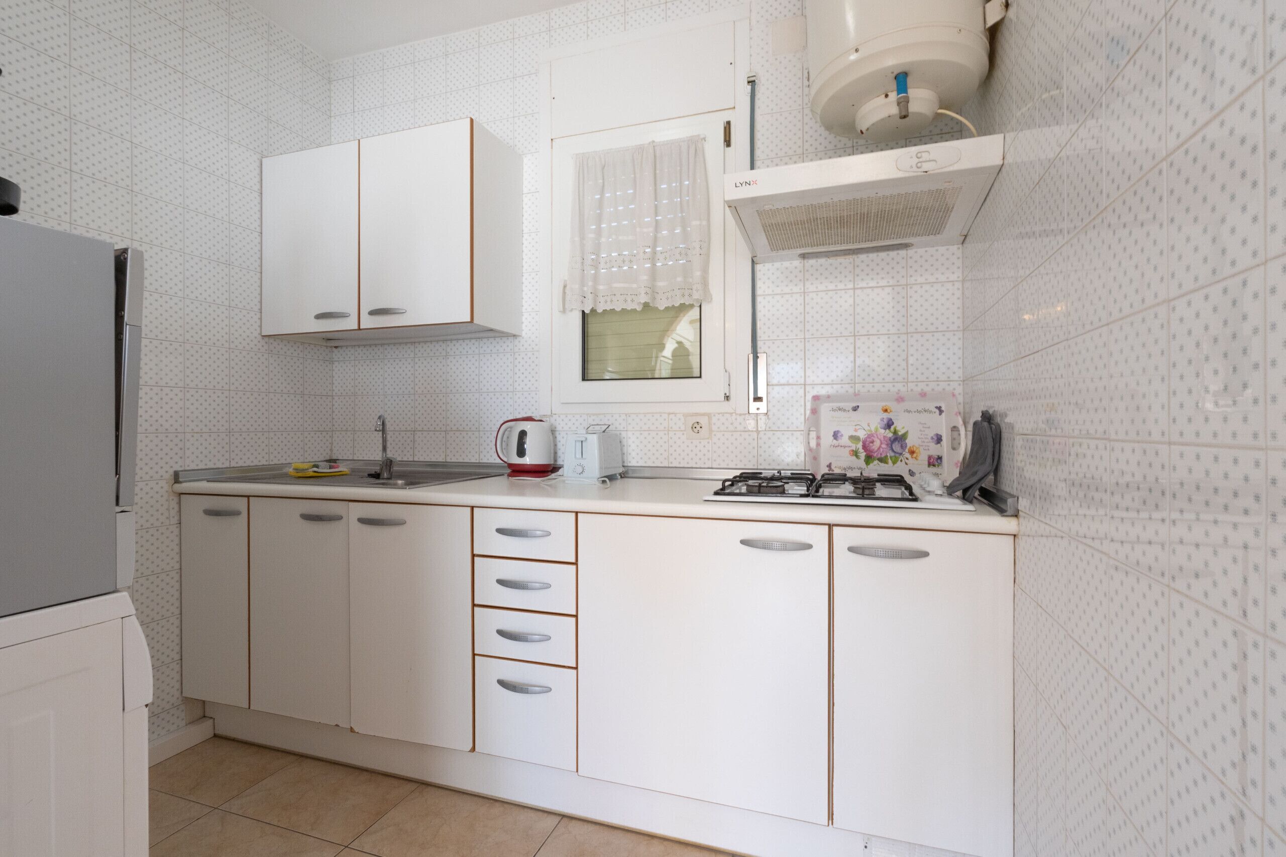A kitchen with white cabinets, a gas stove, a sink, and a window with a curtain.