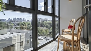 Ein modernes Zimmer mit großen Fenstern und Blick auf die Stadt, ein Holzstuhl, ein kleiner Tisch und ein Blumentopf.