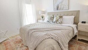 Una camera da letto ordinata con un letto, comodini, una lampada e una finestra con tende.