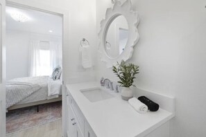A white bathroom with a large mirror, a sink, a potted plant, and a towel. - Weekend Escape on the Coast - Relax & Unwind (Pass Christian)