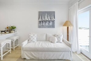 A white living room with a sofa, a painting of sailboats, a lamp, and a view through a window. - Weekend Escape on the Coast - Relax & Unwind (Pass Christian)