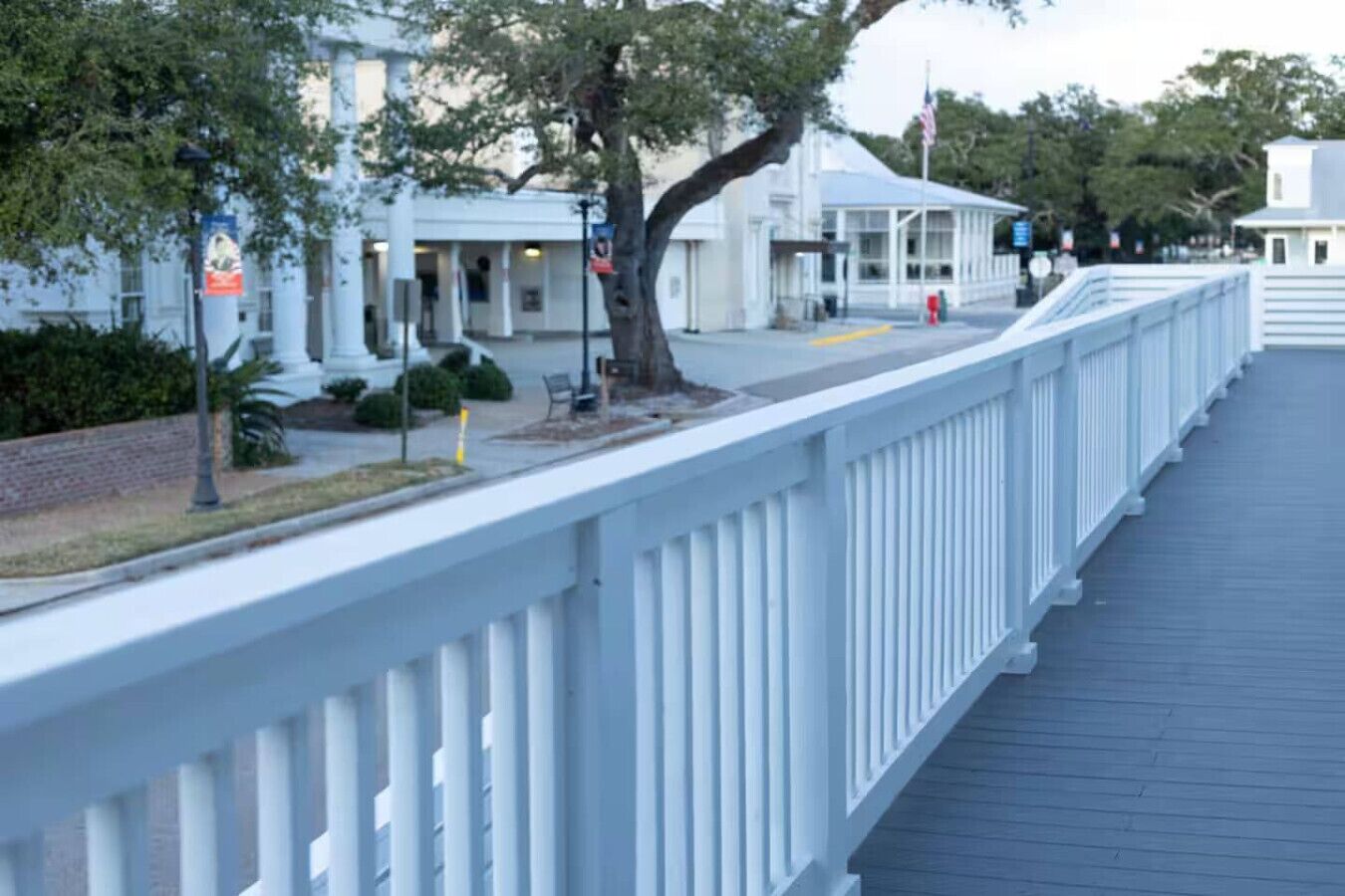 A covered walkway with white railings, leading to a building with a white facade and a blue roof.