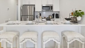 Een moderne keuken met witte kastjes, roestvrijstalen apparatuur en een centraal eiland met barkrukken.