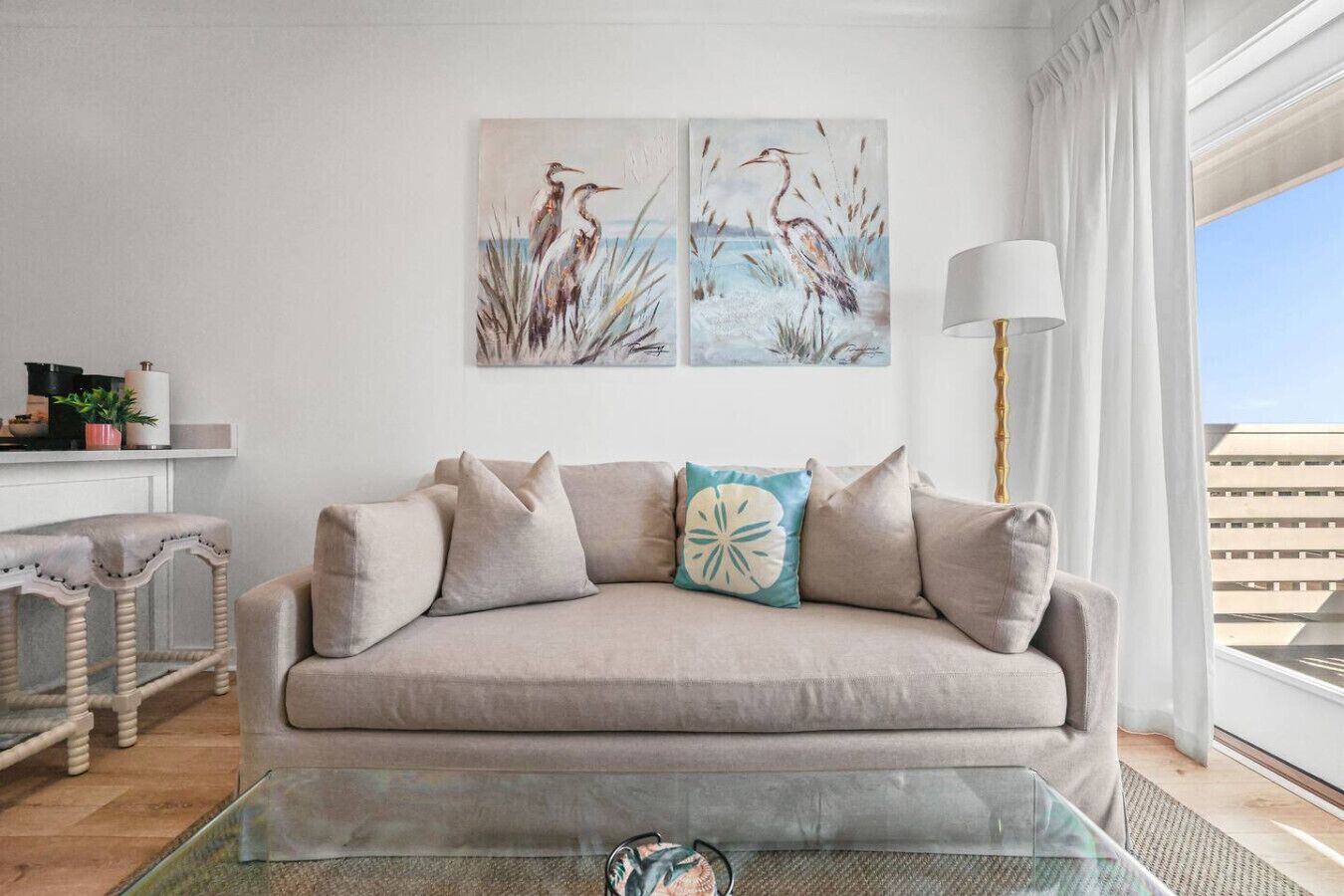 A living room with a beige sofa, a glass coffee table, and two wall-mounted paintings of birds.