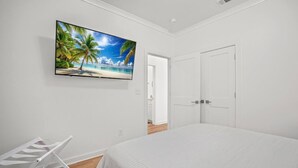 Une chambre avec un lit, un téléviseur fixé au mur, une porte blanche et une chaise blanche.