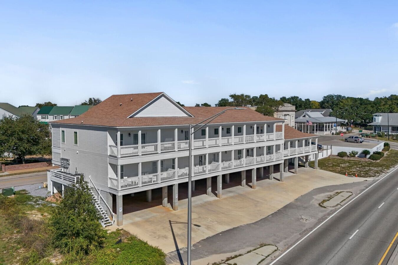 A two-story building with a balcony on the ground floor, a parking lot in front, and a road nearby.