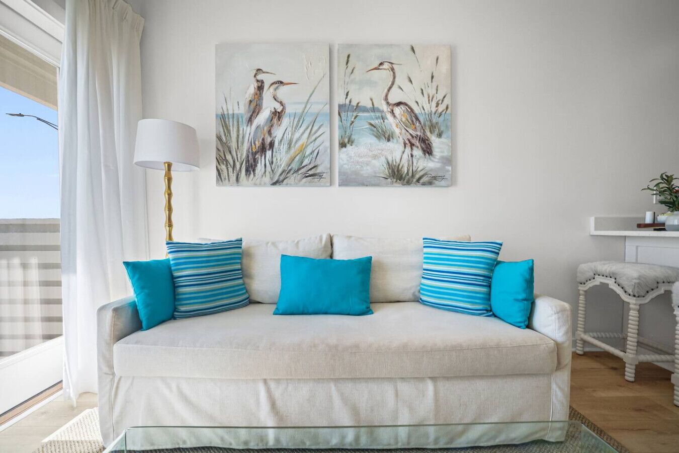 Ein Wohnzimmer mit einer Couch, blauen Kissen, einer Lampe und zwei Wandbildern mit Vogelmotiven.