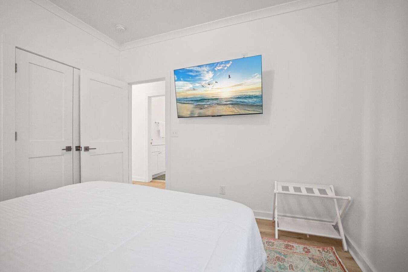 Un dormitori amb un llit, un armari blanc, una panxa blanca i una pintura d'una escena de platja.