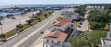 A coastal road with a marina, a white building with a red roof, and residential houses in the background.
