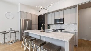 A modern kitchen with a central island, stainless steel appliances, and bar stools. - Pass Christian 3BR Townhome - Pool - Sleeps 6 (Pass Christian)