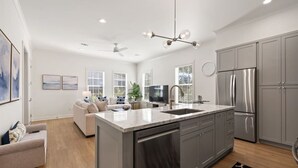 A modern kitchen with a central island, stainless steel appliances, and a dining area with a sofa and coffee table. - Pass Christian 3BR Townhome - Pool - Sleeps 6 (Pass Christian)