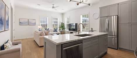 A modern kitchen with a central island, stainless steel appliances, and a dining area with a sofa and coffee table.