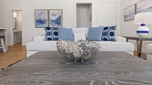 A modern living room with a white sofa, patterned cushions, a decorative bowl on a wooden table, and abstract wall art. - Pass Christian 3BR Townhome - Pool - Sleeps 6 (Pass Christian)