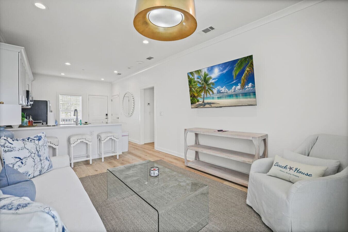 A modern living room with a white sofa, a coffee table, and a TV stand. A painting of a beach scene is on the wall.