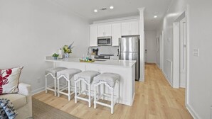 A modern kitchen with white cabinets, a stainless steel refrigerator, and a bar area with white stools. - Extended Stay Friendly-Full Kitchen & Laundry (Pass Christian)