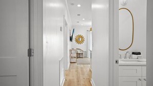 A hallway with a wooden floor leading to a room with a bed, a mirror, and a vanity with a sink. - Extended Stay Friendly-Full Kitchen & Laundry (Pass Christian)