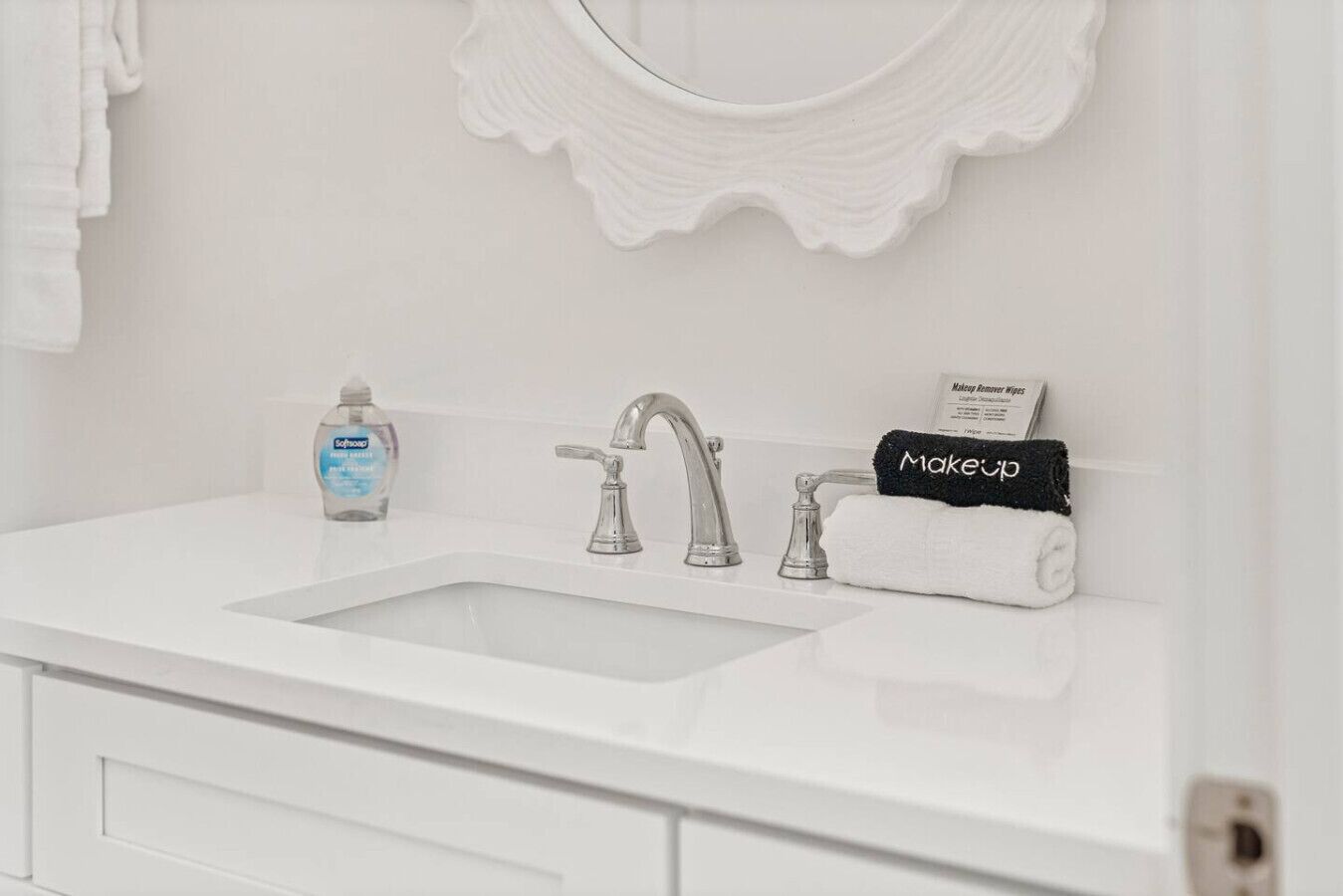 A white bathroom sink with a mirror above it, a bottle of soap, and a towel with "Makeup" on it.