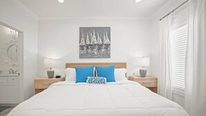 A neatly arranged bedroom with a large bed, two bedside tables with lamps, a wall-mounted painting, and a window with curtains. - Extended Stay Friendly-Full Kitchen & Laundry (Pass Christian)