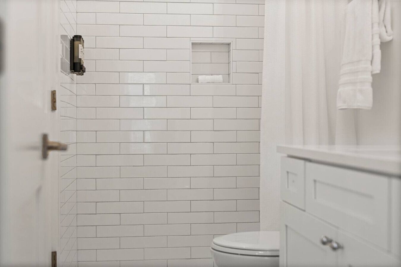 Un bagno con piastrelle bianche tipo metro, un water bianco e un asciugamano appeso al muro.