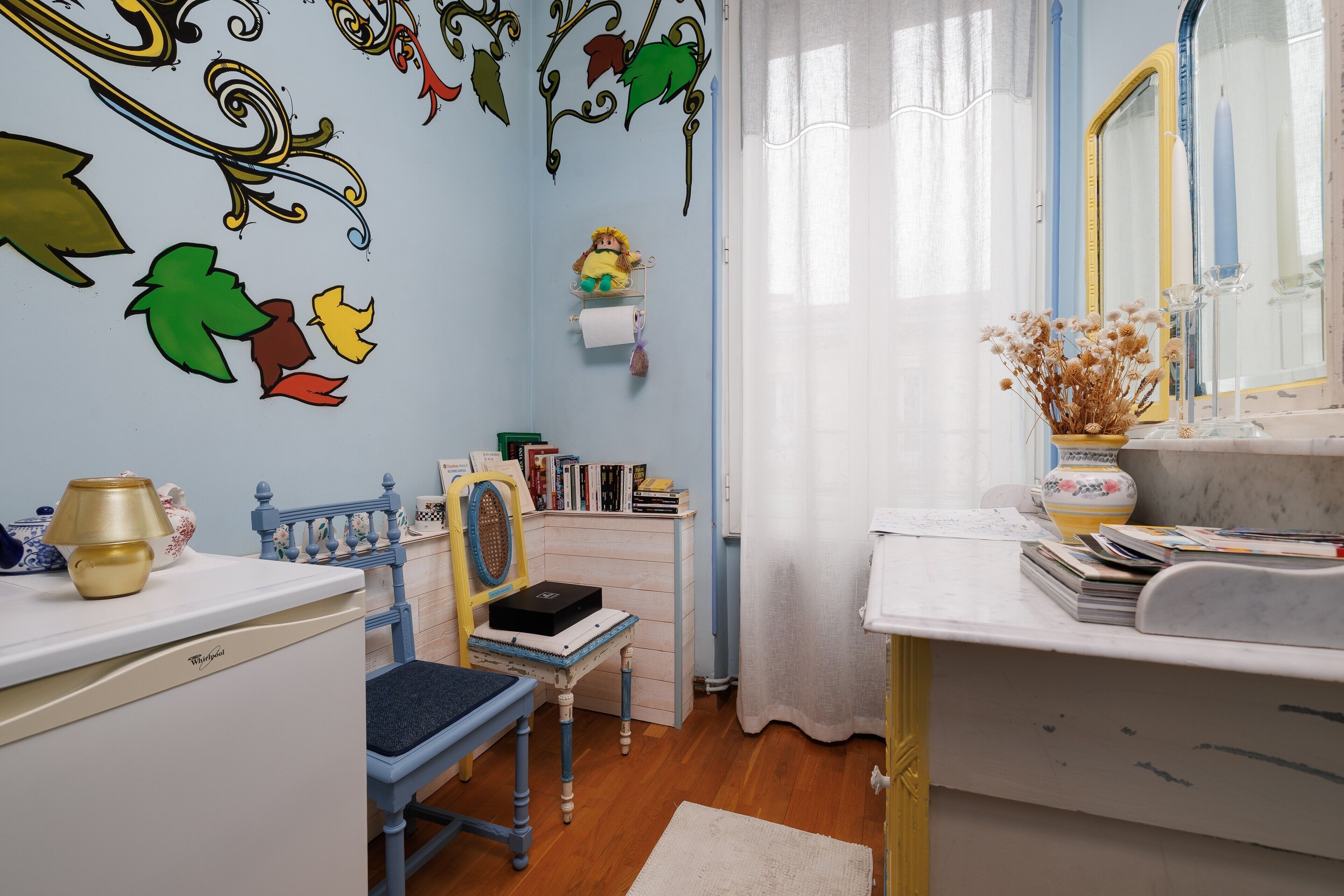 A room with a desk, chair, bookshelf, decorative wall art, and a mirror.