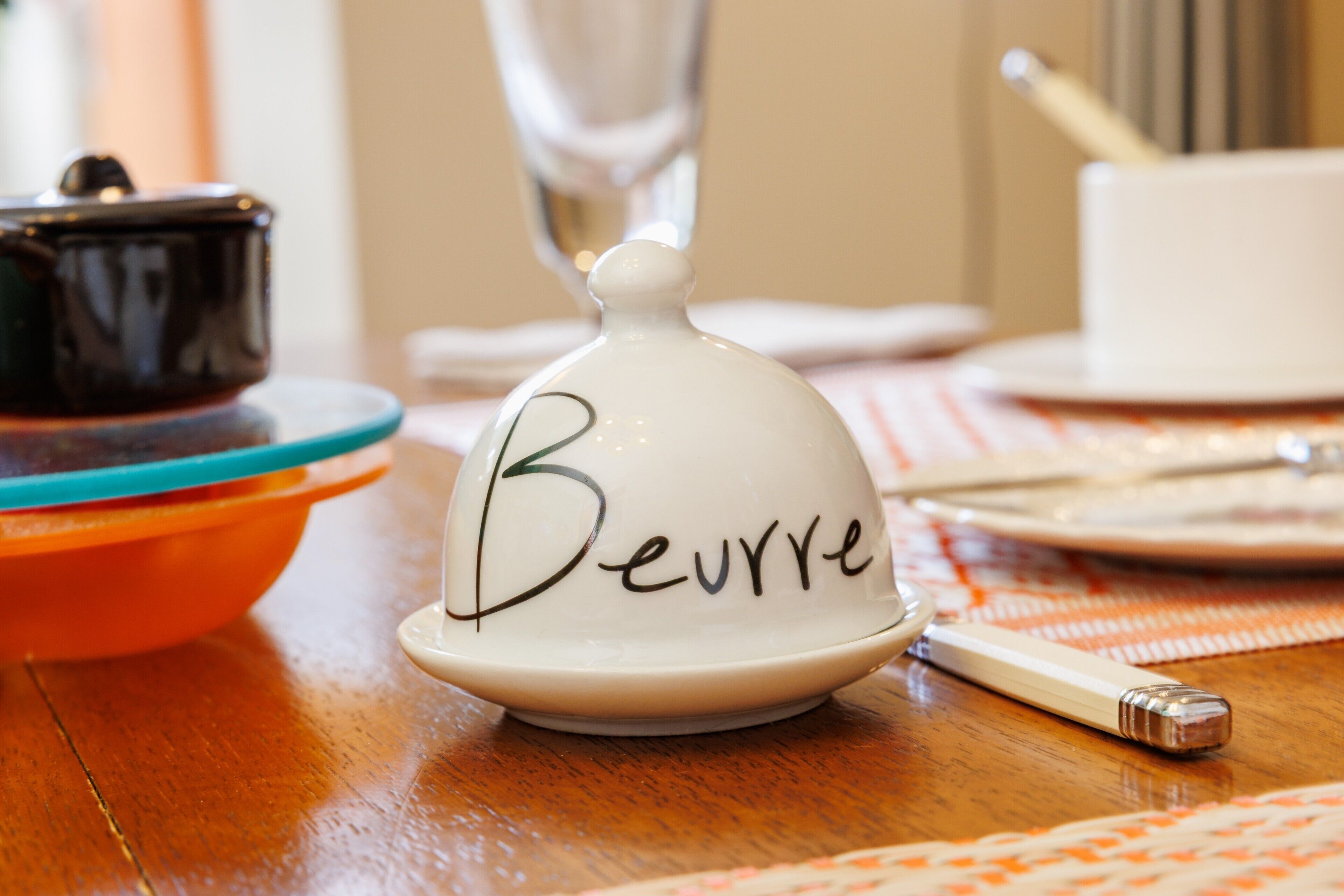 Une table avec un sucrier blanc portant l’étiquette « Beurre », un récipient noir et une tasse blanche.
