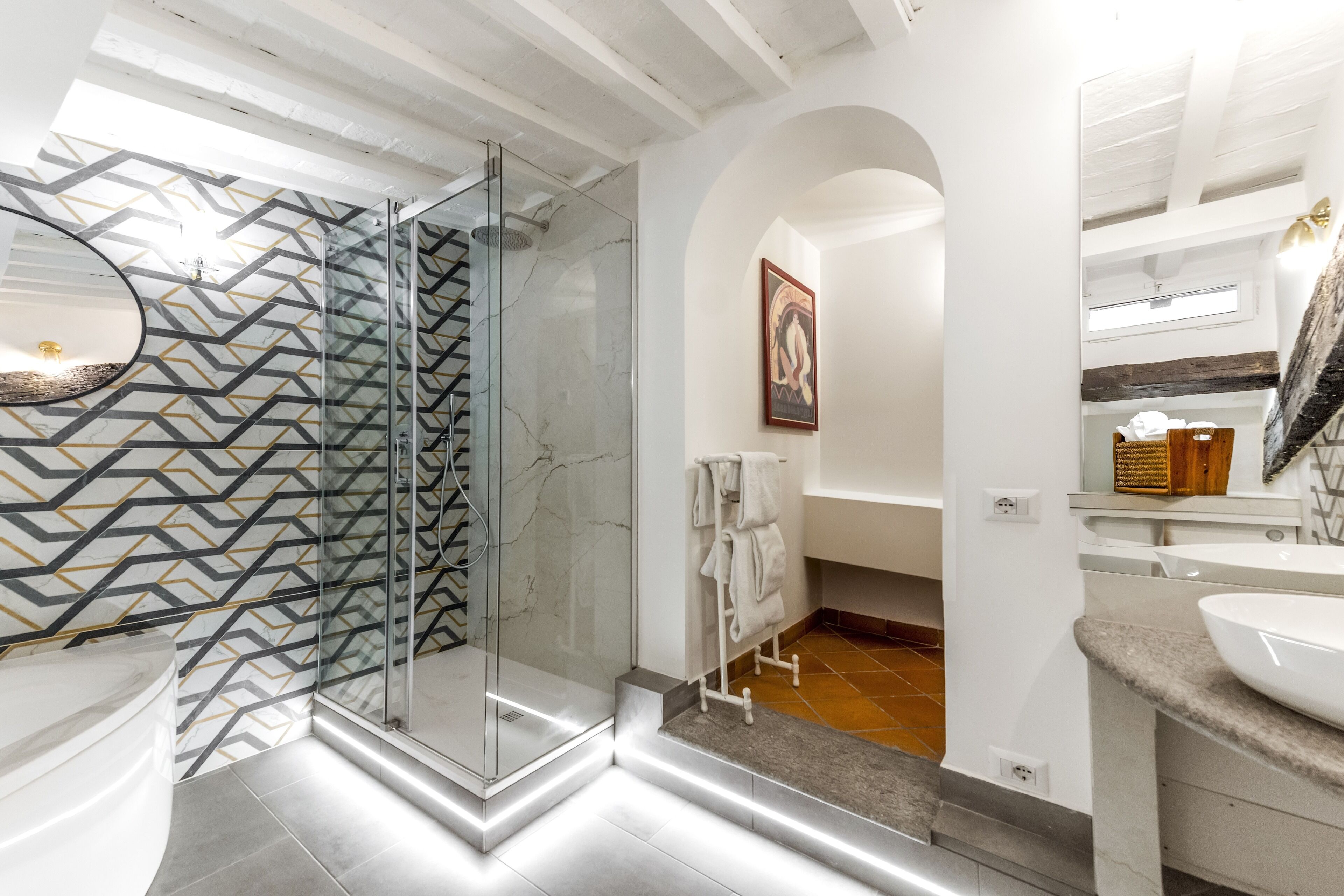 Une salle de bain moderne avec une douche en verre, un mur aux motifs de marbre, un lavabo blanc et un miroir.