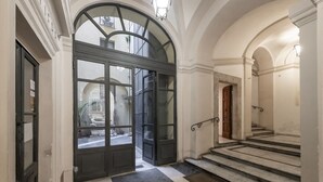 A grand entrance with a large arched doorway, a staircase leading to an upper floor, and a view of the street outside. - Cestari Luxury Terraces (Rome)