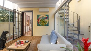 A modern living room with a sofa, a coffee table, and a decorative dog statue. There is a staircase with a metal railing and a colorful painting on the wall. - Cestari Luxury Terraces (Rome)