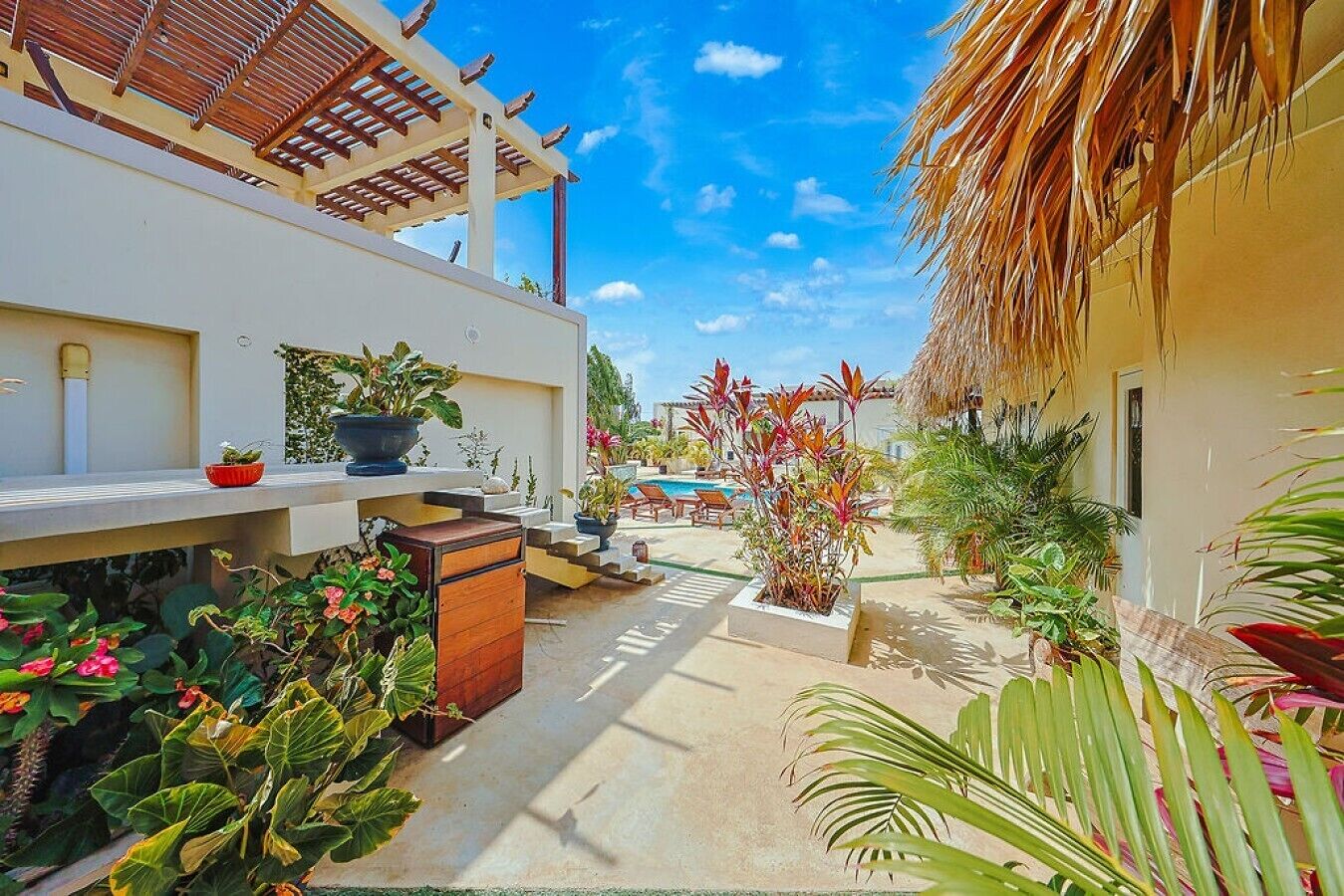 A covered outdoor area with a pool, potted plants, and a wooden bench.